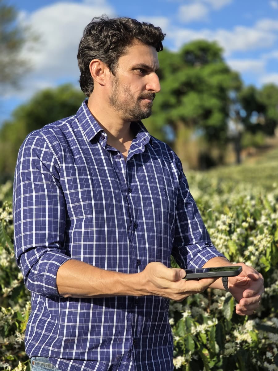 Fábio Kinsch consultando o celular no meio da lavoura de café